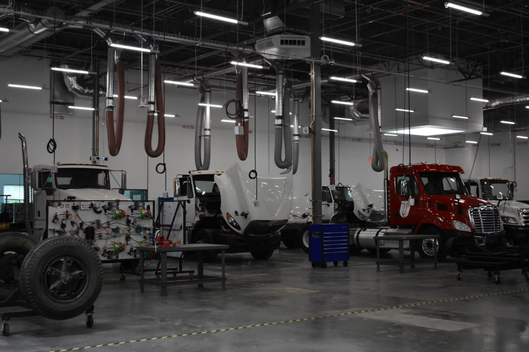 Industrial truck repair shop with white and red semi-trucks, open engine bays, and overhead hoses in a large service bay